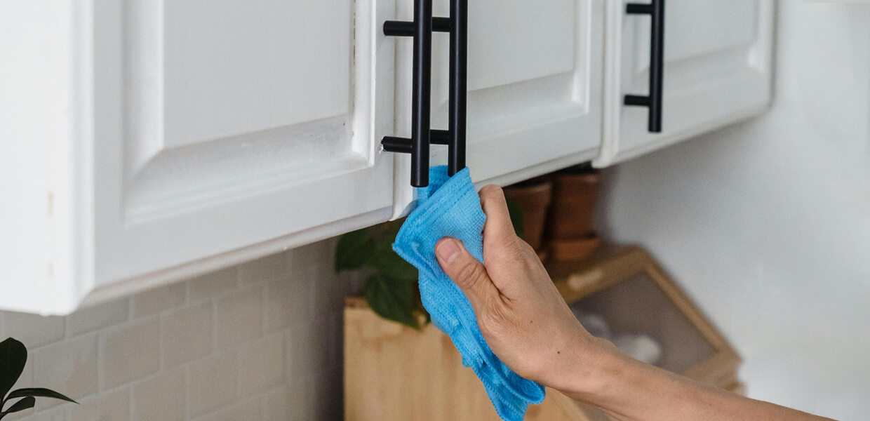 a man cleaning kitchen cabinet handles using a blue microfibre cloth