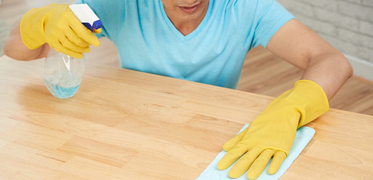 a man scrubbing a wooden worktop wearing yellow rubber gloves